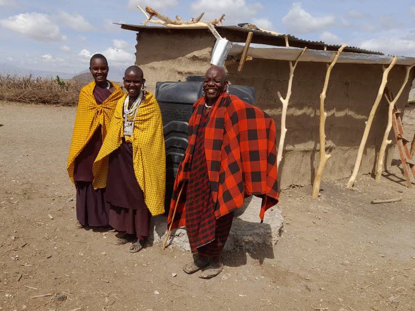 Two Maasai women and one man standing with their 1,000-liter water tank
